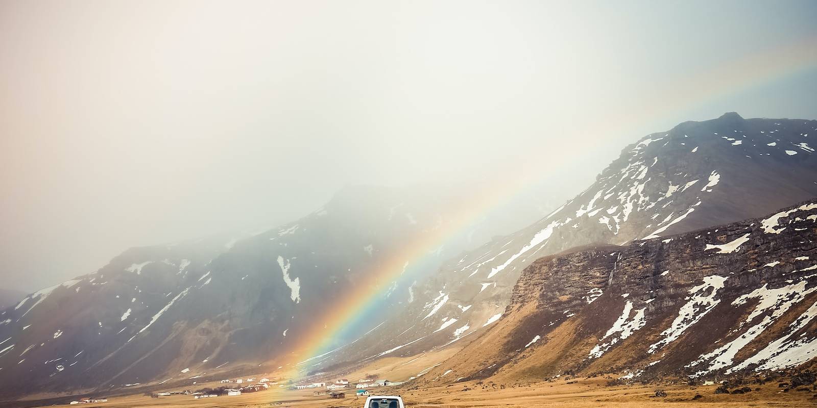 white car travelling near mountains with rainbow
